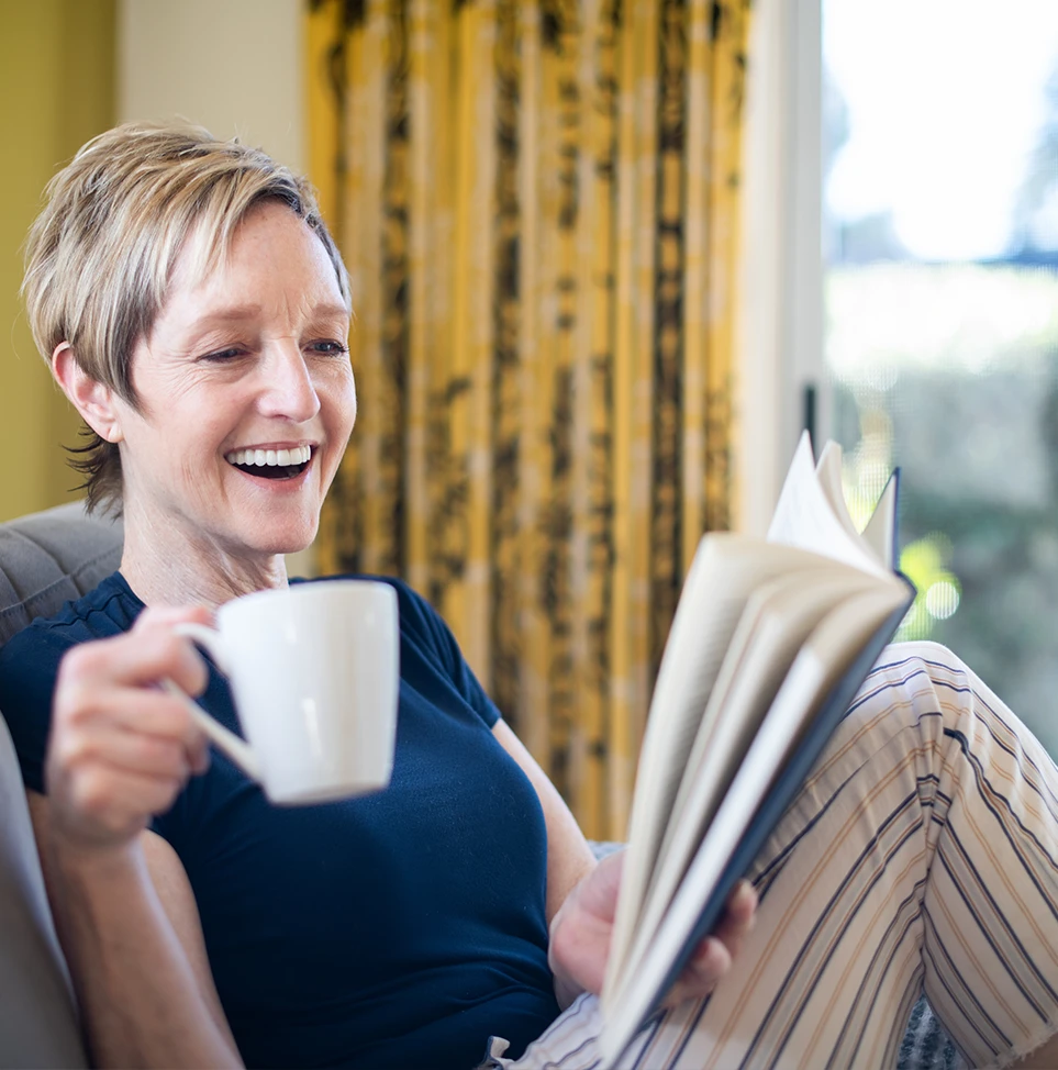 a smiling women with a coffee mug and a book